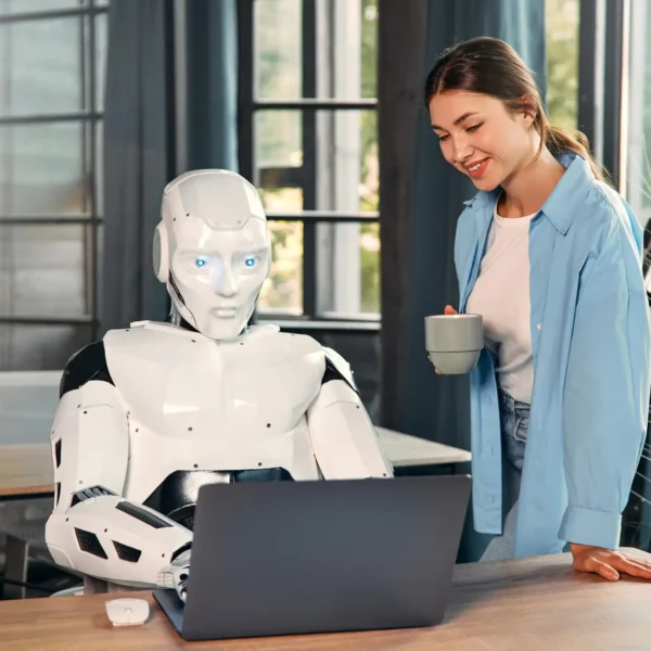 Young woman with a cup of coffee and a humanoid robot working while sitting at a laptop in a modern office. Collaboration between humans and artificial intelligence.