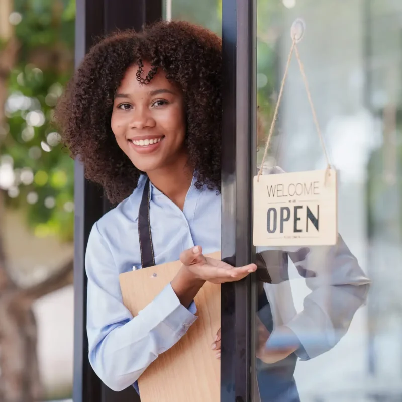 Young Female manager in restaurant with notebook. Woman coffee shop owner with open sign. Small business concept.